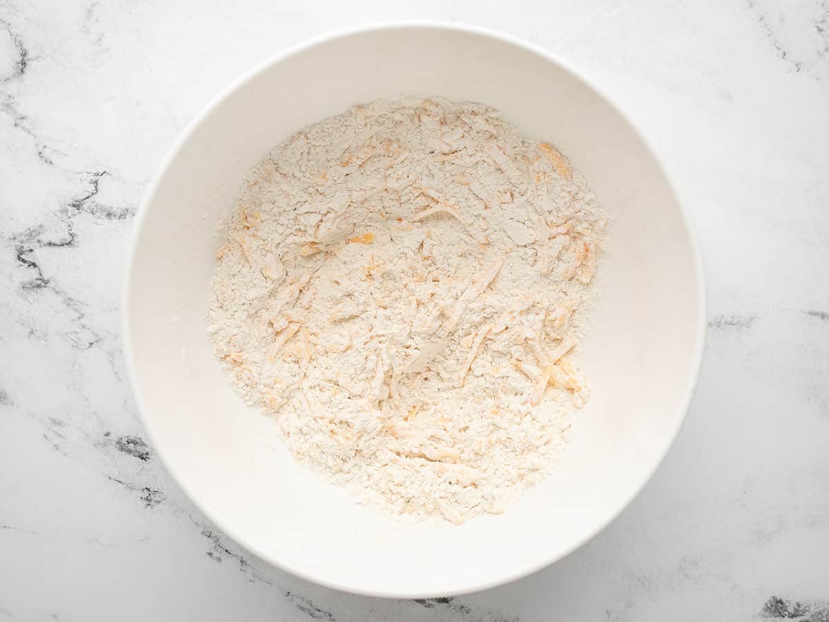 Overhead view of dry ingredients to make cheddar biscuits with cheese coated in the flour.