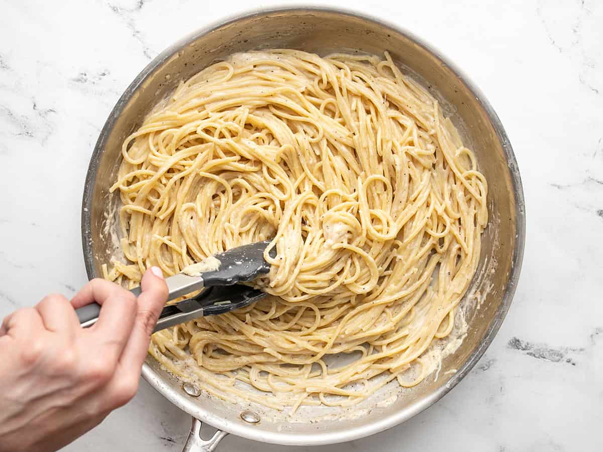 Overhead shot of finished Cacio e Pepe in a pan with tongs in it.