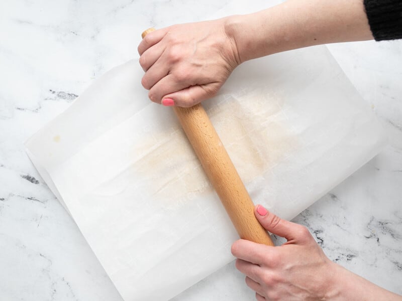 Overhead shot of sugar cookie dough being rolled out between two sheets of parchment.