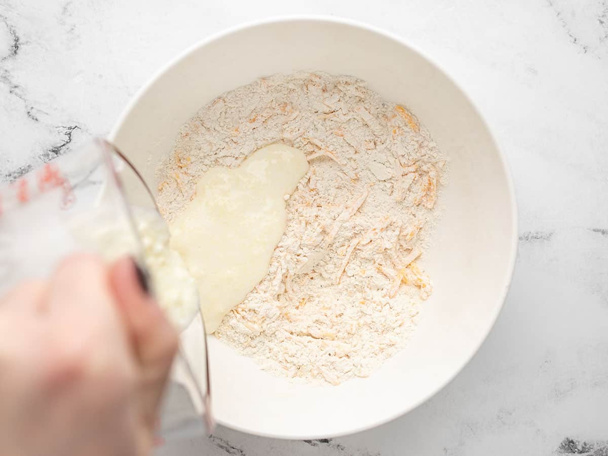 Cook pours mixed buttermilk and melted butter into a while bowl with dry ingredients to make cheddar biscuits. 
