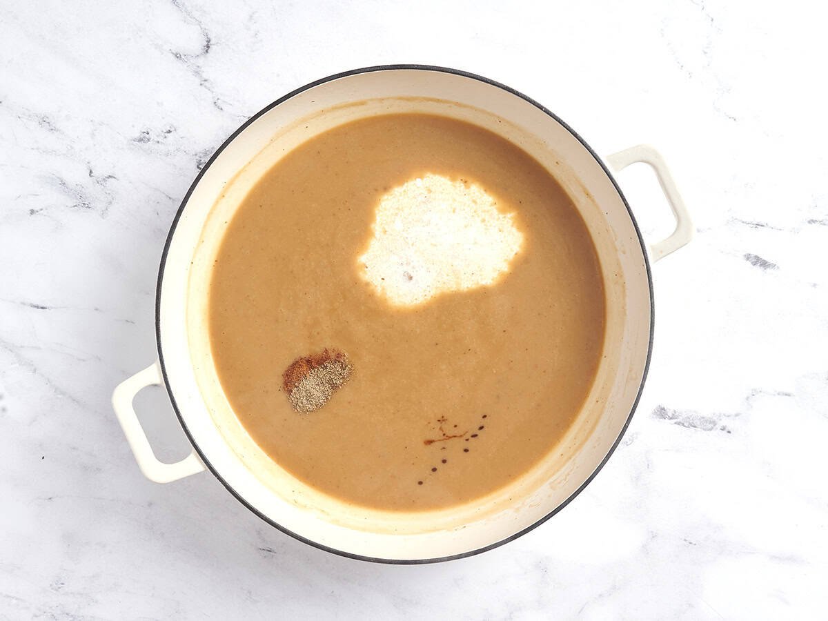 Spices and cream added to a roux in a pot to make a creamy sauce.