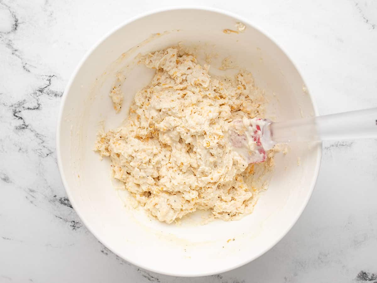 Overhead view of raw cheddar drop biscuit dough with a red spatula.