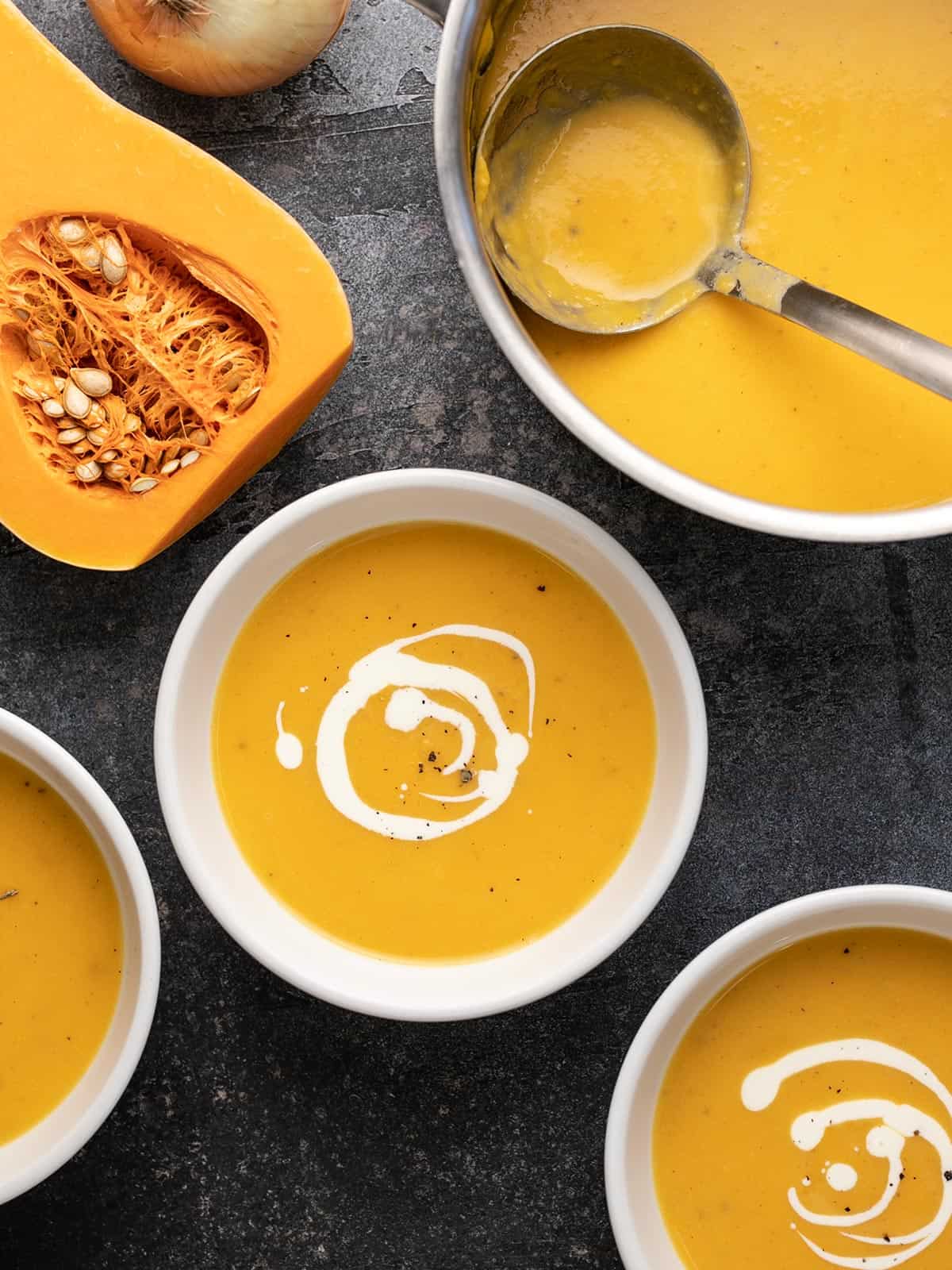 Butternut squash being served from the pot into white bowls. 