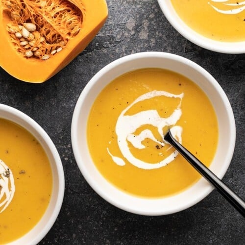 Overhead view of three bowls of butternut squash soup with cream swirled on top.