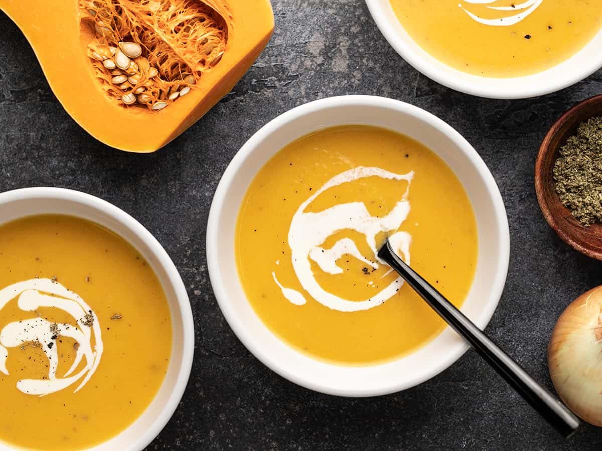 Overhead view of three bowls of butternut squash soup with cream swirled on top.