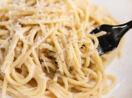 Side shot of finished Cacio e Pepe on a plate with a fork in it.