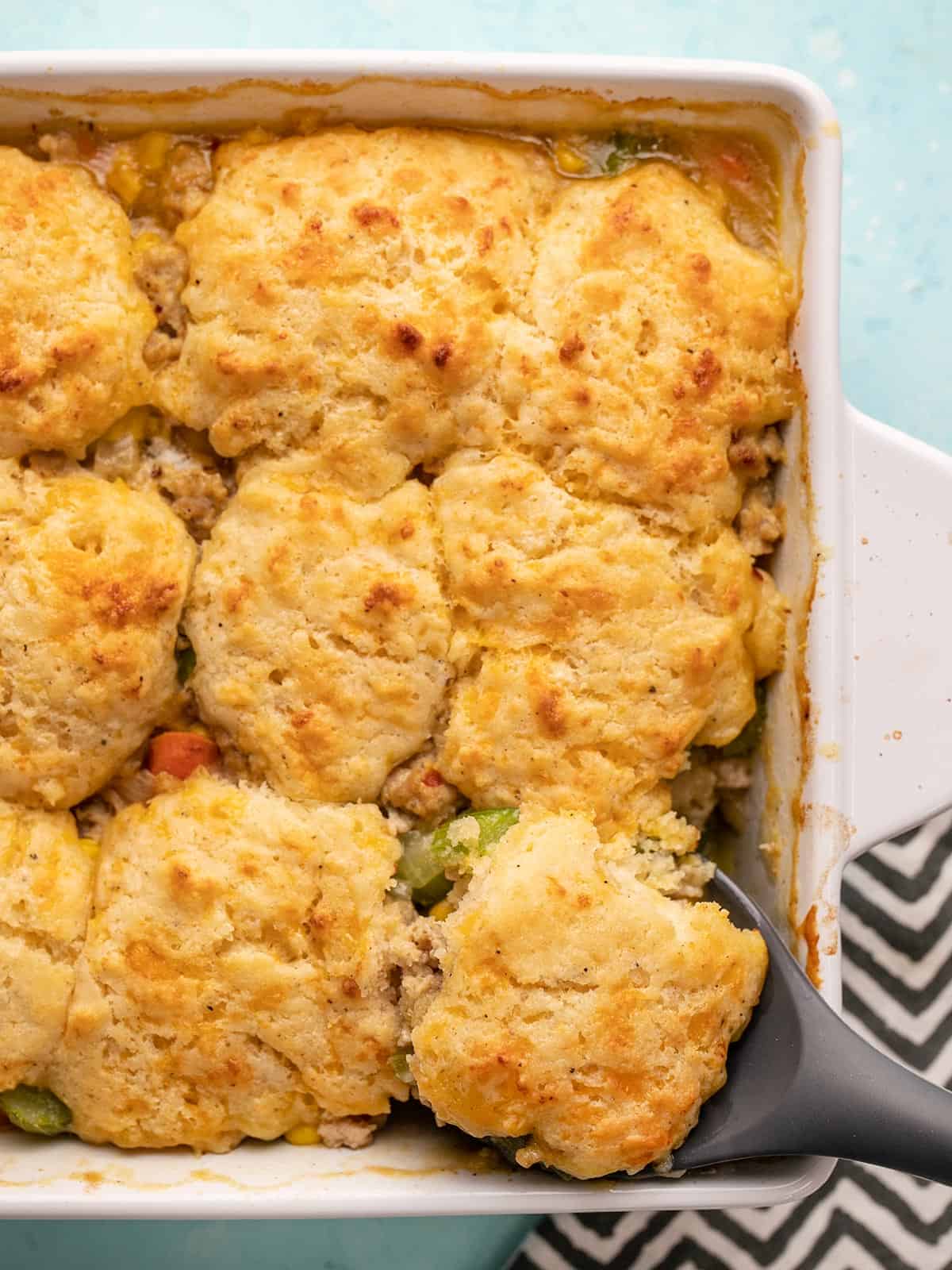 Overhead view of cooked chicken and biscuit casserole with a serving spoon
