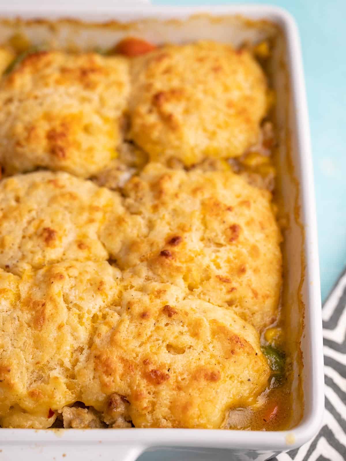 Side view of cooked chicken and biscuit casserole in a white casserole dish.