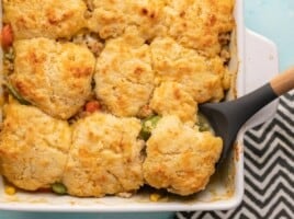 Cooked chicken and biscuit casserole in a casserole dish with a serving spoon.