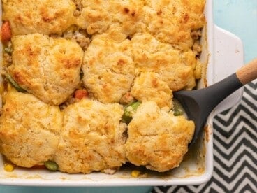 Cooked chicken and biscuit casserole in a casserole dish with a serving spoon.