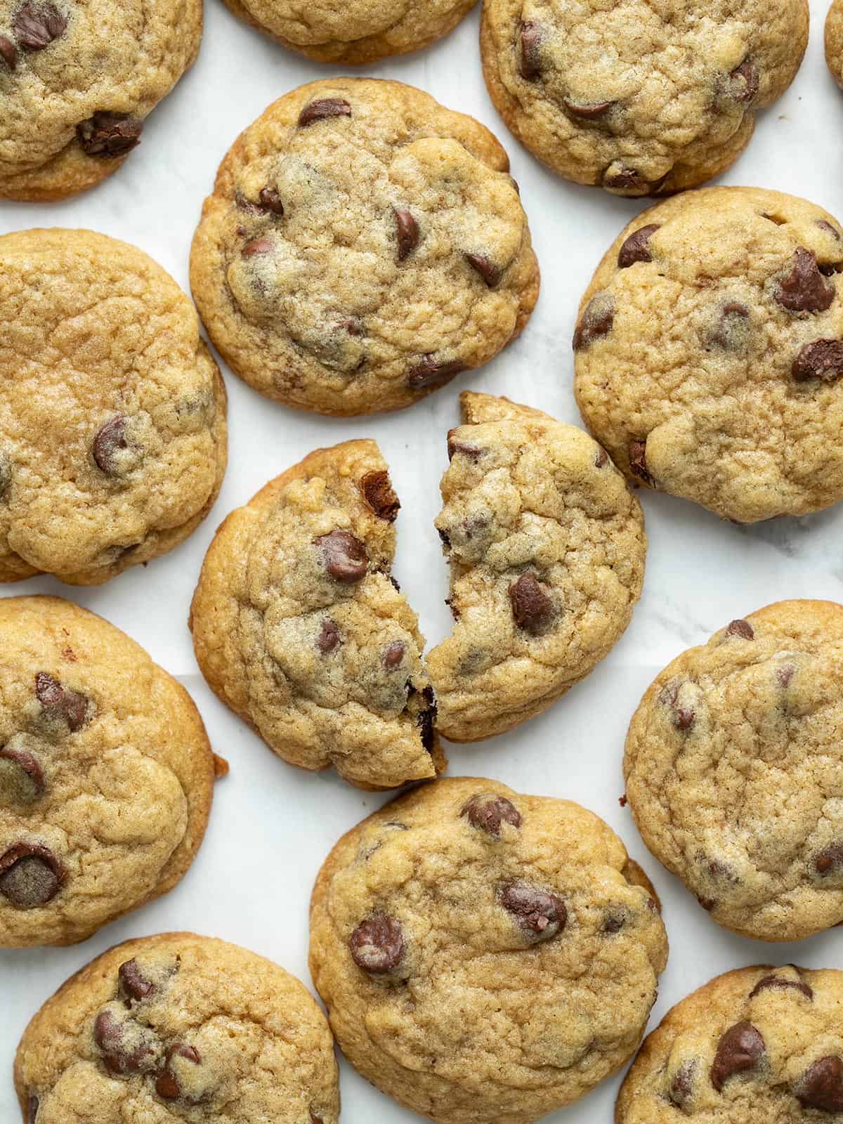 Overhead shot of chocolate chip cookies on a sheet pan with one of the cookies torn in half.