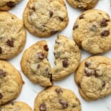 Overhead shot of chocolate chip cookies on a sheet pan with one of the cookies torn in half.