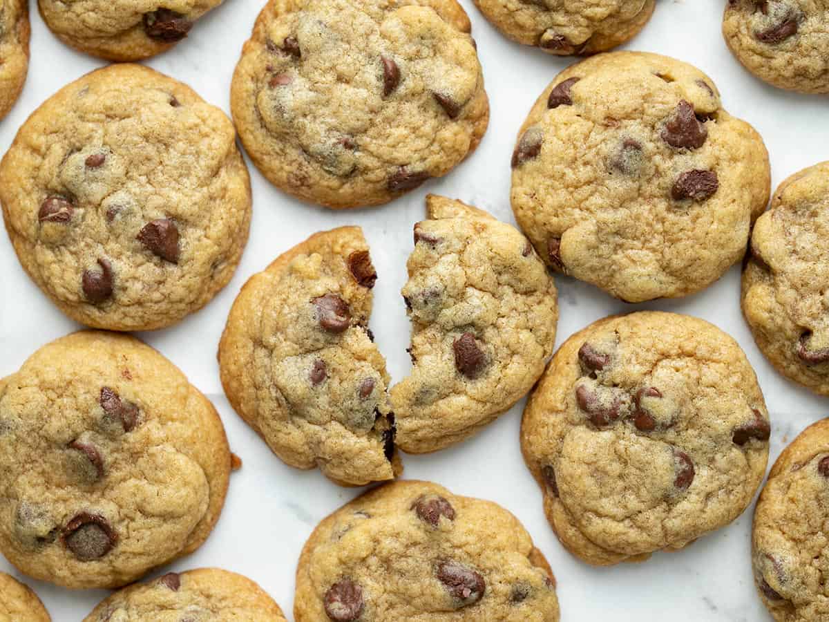 Overhead shot of chocolate chip cookies on a sheet pan with one of the cookies torn in half.