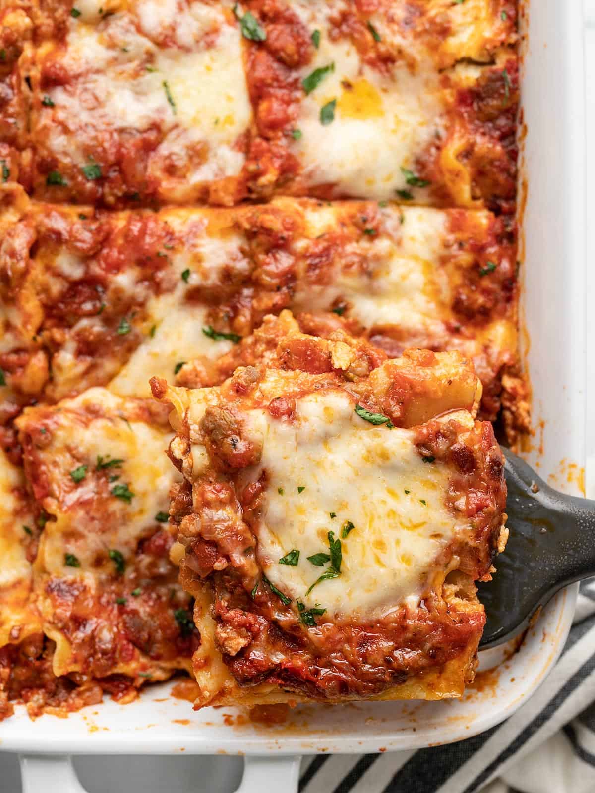 Overhead view of a sliced lasagna with one slice being lifted from the pan.