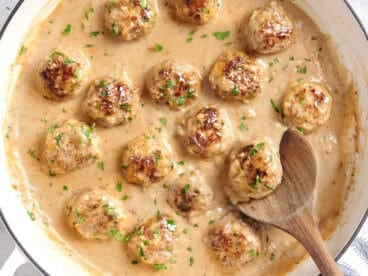Overhead view of swedish meatballs in a skillet with a wooden spoon.
