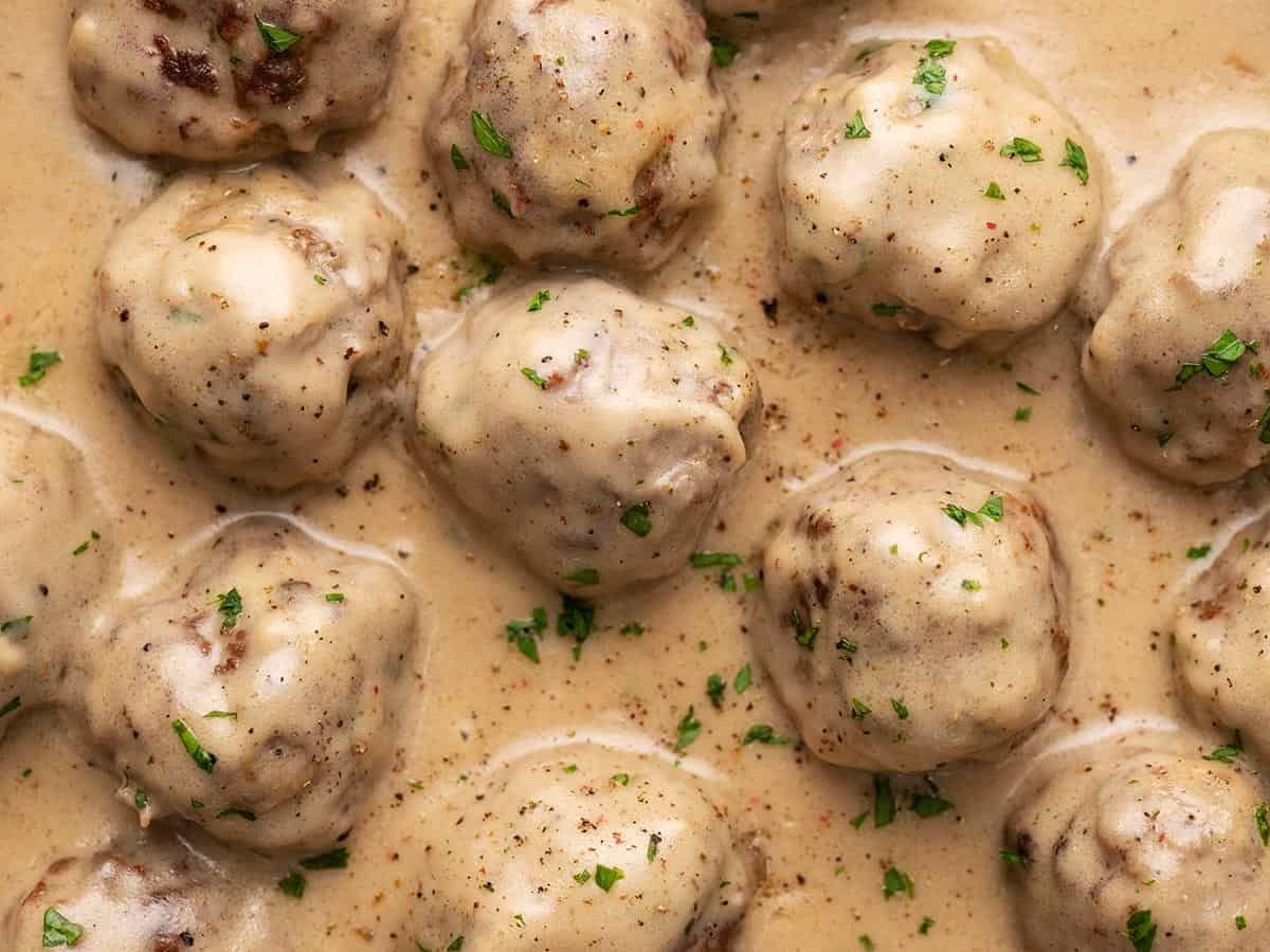 Close up overhead view of meatballs in sauce garnished with parsley. 