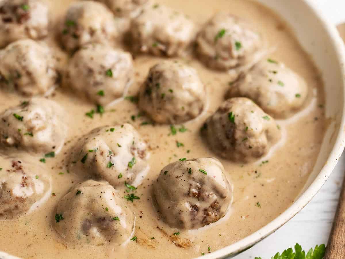 Close up side view of a skillet full of Swedish Meatballs in cream sauce.