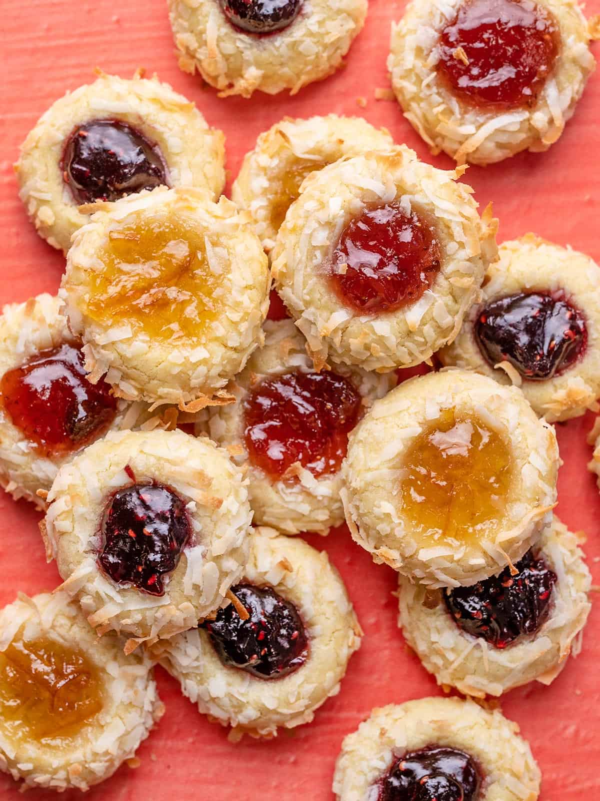 A pile of jam thumbprint cookies with different colors of jam.
