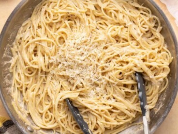 Overhead shot of finished Cacio e Pepe in a pan with tongs in it.