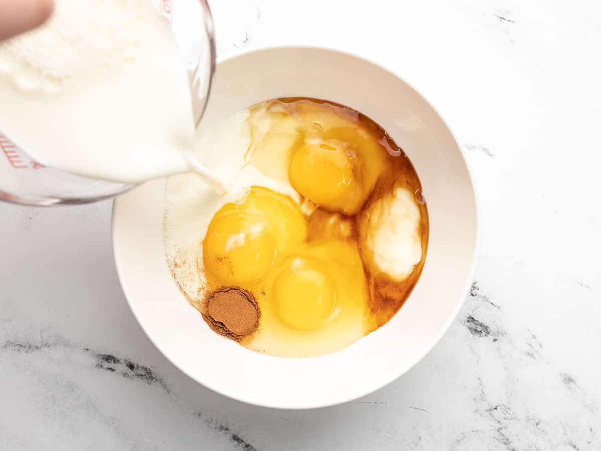 Tous les ingrédients de la crème anglaise sont ajoutés à un bol blanc dans lequel on verse du lait.