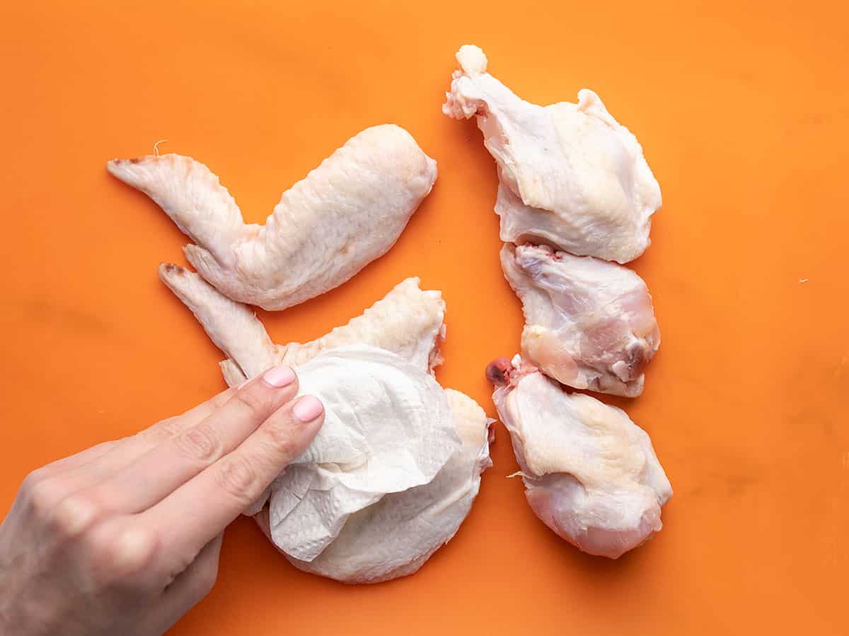 Overhead shot of a hand patting raw chicken wings dry with a paper towel.
