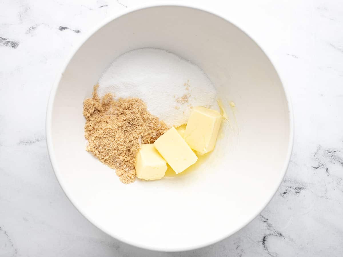 White sugar and brown sugar with softened butter in a white bowl.