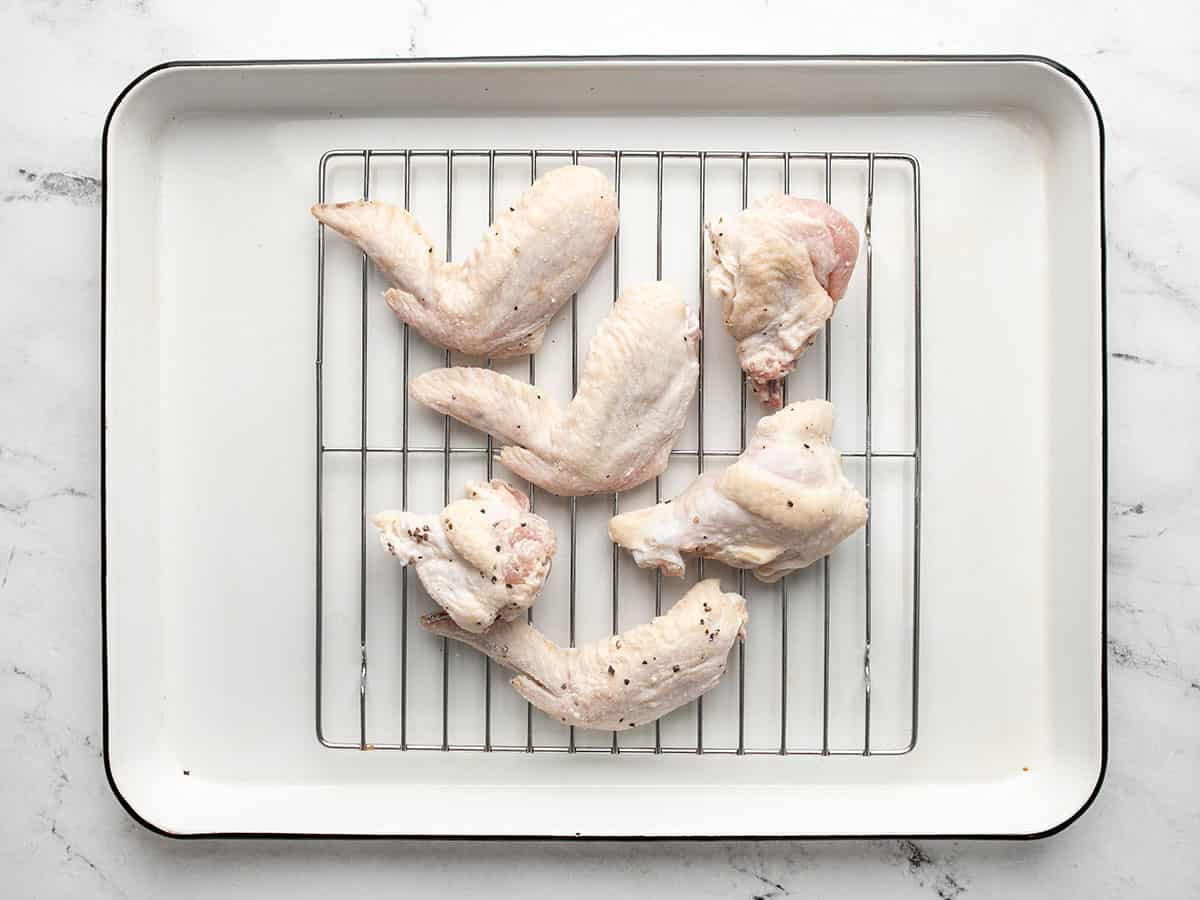Overhead shot of raw chicken wings rubbedin salt and baking powder on a sheet pan rack.