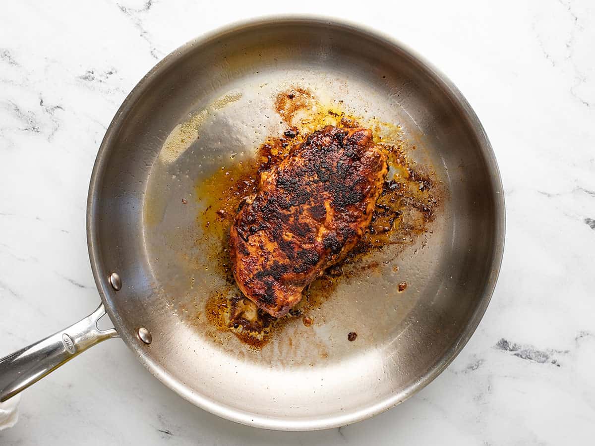 Overhead shot of a blackened chicken breast in a stainless steel skillet.
