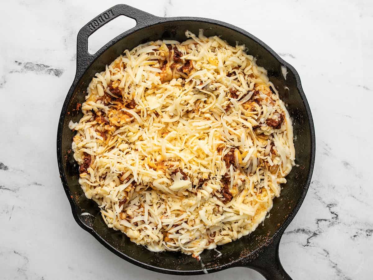 Overhead shot of chorizo topped with shredded cheese in a cast iron pan.