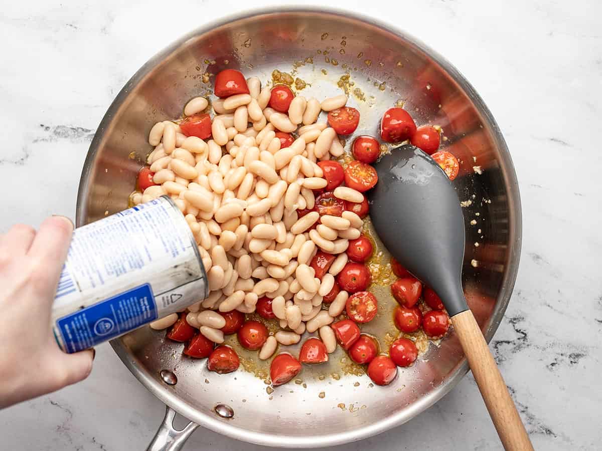 White beans being poured into the skillet.