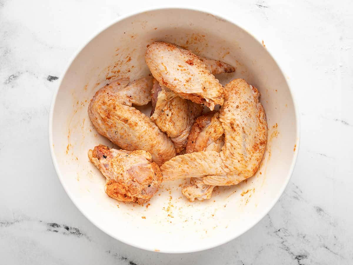 Overhead shot of raw wings tossed with spices in a white bowl.