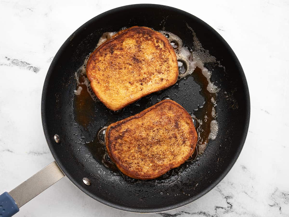 Two pieces of french toast in a pan after cooking.