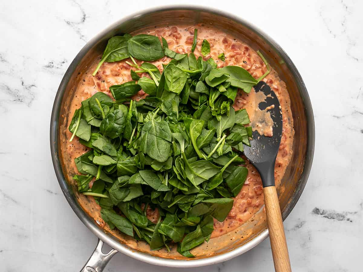 Fresh spinach added to the sauce in the skillet.