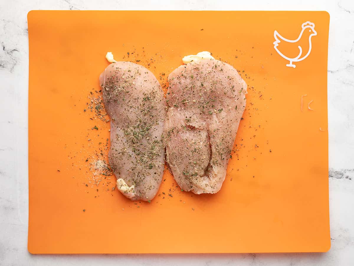 Seasoned chicken breast on an orange cutting board.