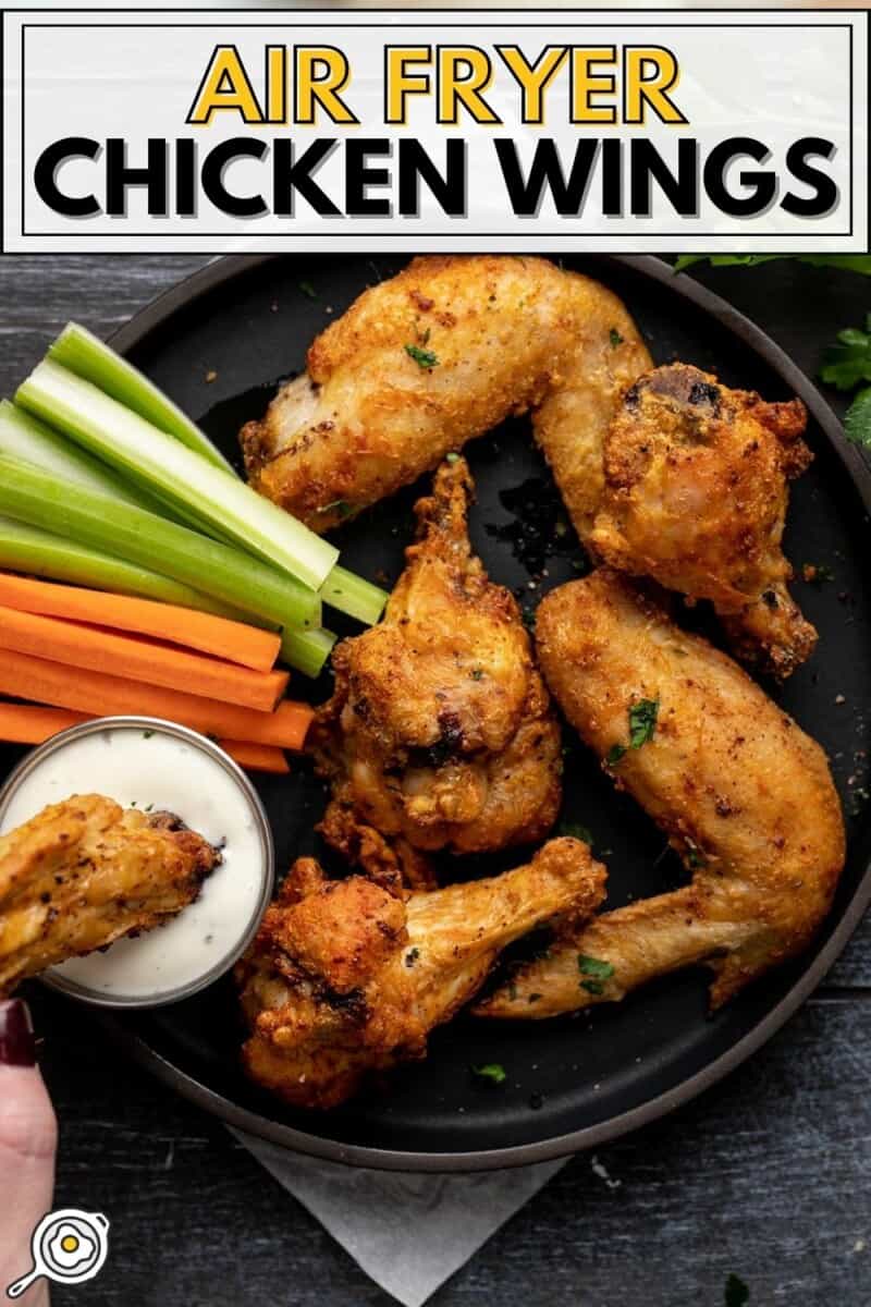 Overhead view of a plate full of air fryer chicken wings, one being dipped into ranch.
