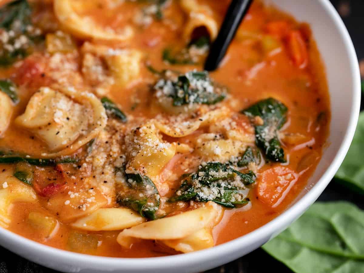 Close up side view of a bowl of creamy tortellini soup garnished with Parmesan.