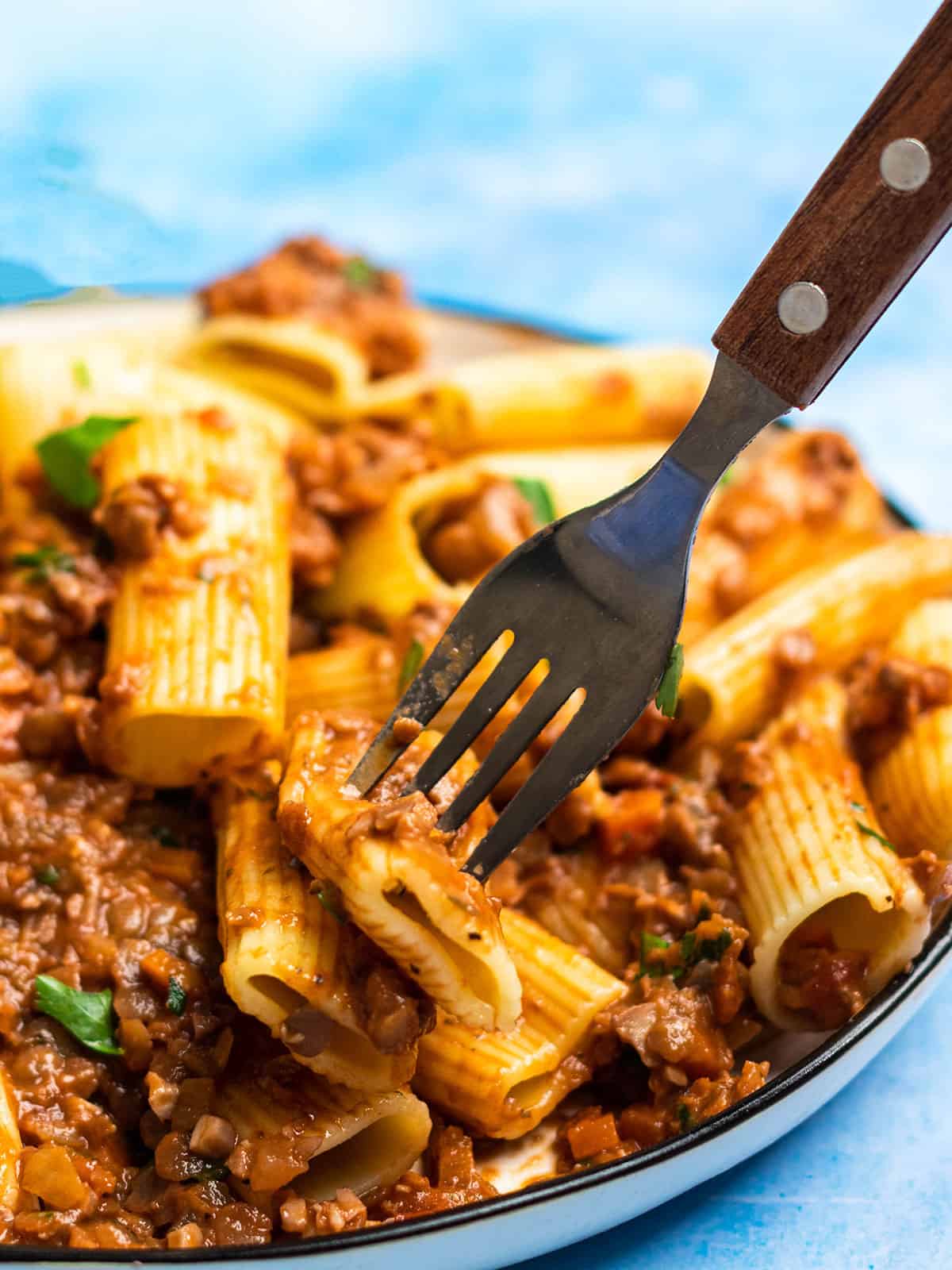 close up side view of lentil bolognese on a plate of rigatoni being pierced with a fork.