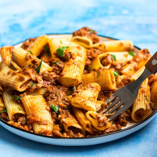 Side view of a plate full of pasta and lentil bolognese with a fork in the side.