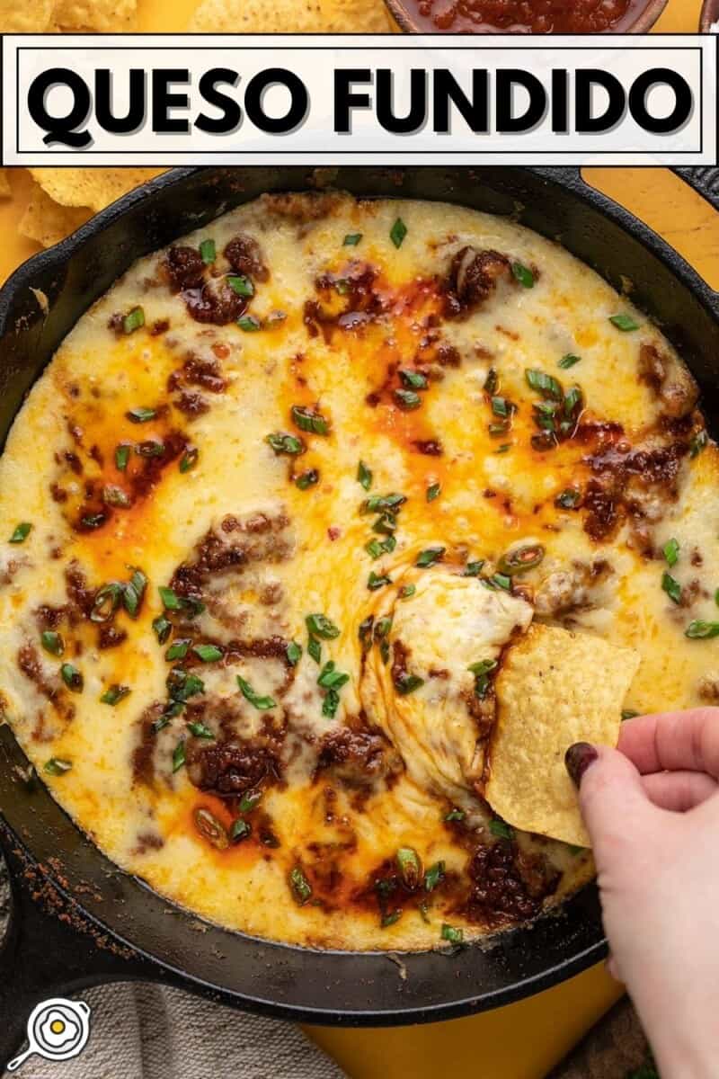 Overhead view of a chip being dipped into a skillet full of queso fundido.