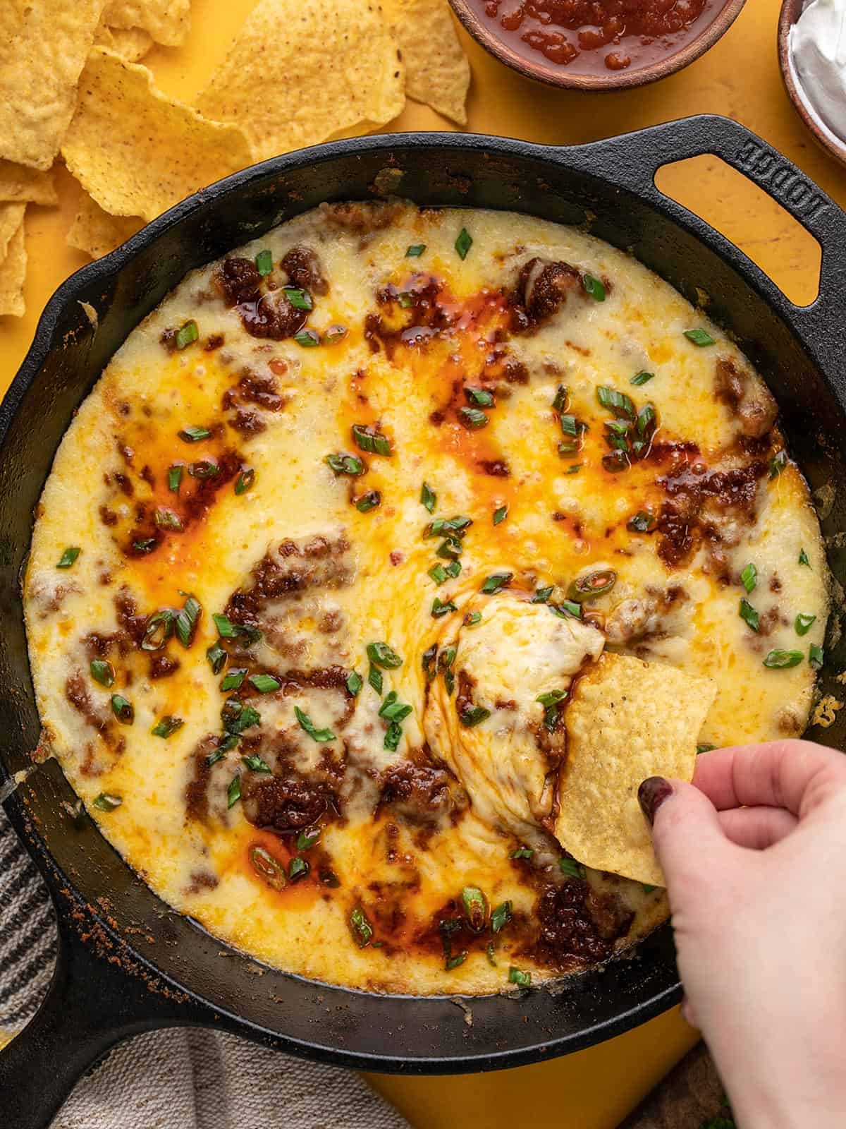 Overhead shot of Queso Fundido in a cast iron pan  with a hand dipping a chip into it.