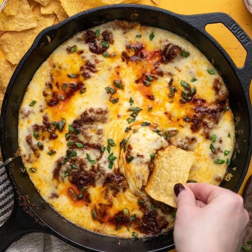 Overhead shot of Queso Fundido in a cast iron pan with a hand dipping a chip into it.
