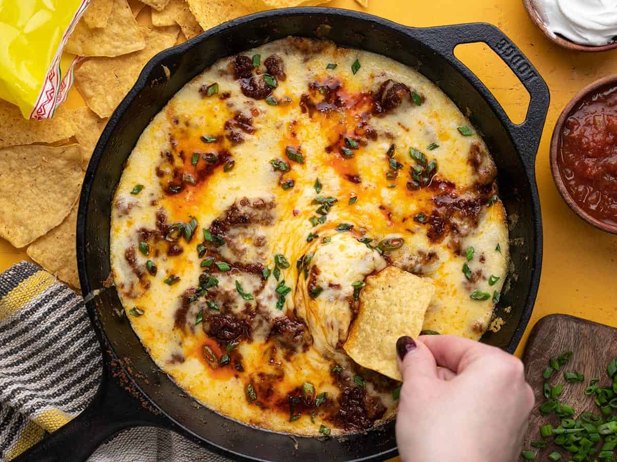 Overhead shot of Queso Fundido in a cast iron pan with a hand dipping a chip into it.