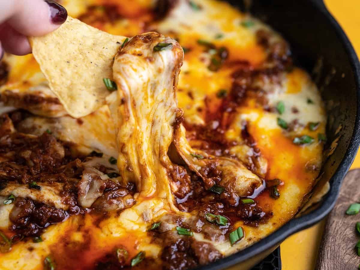 Side shot of Queso Fundido in a cast iron pan with a hand dipping a chip into it.