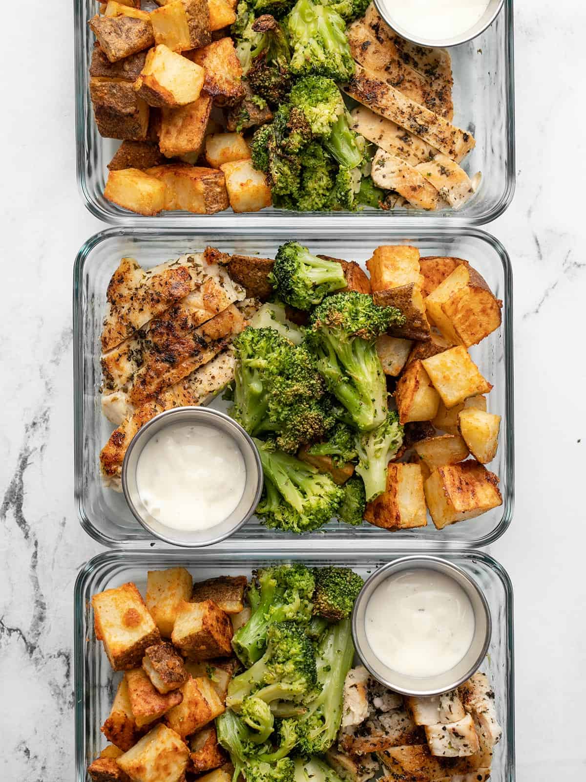 Chicken, potatoes, and broccoli divided into glass meal prep containers.