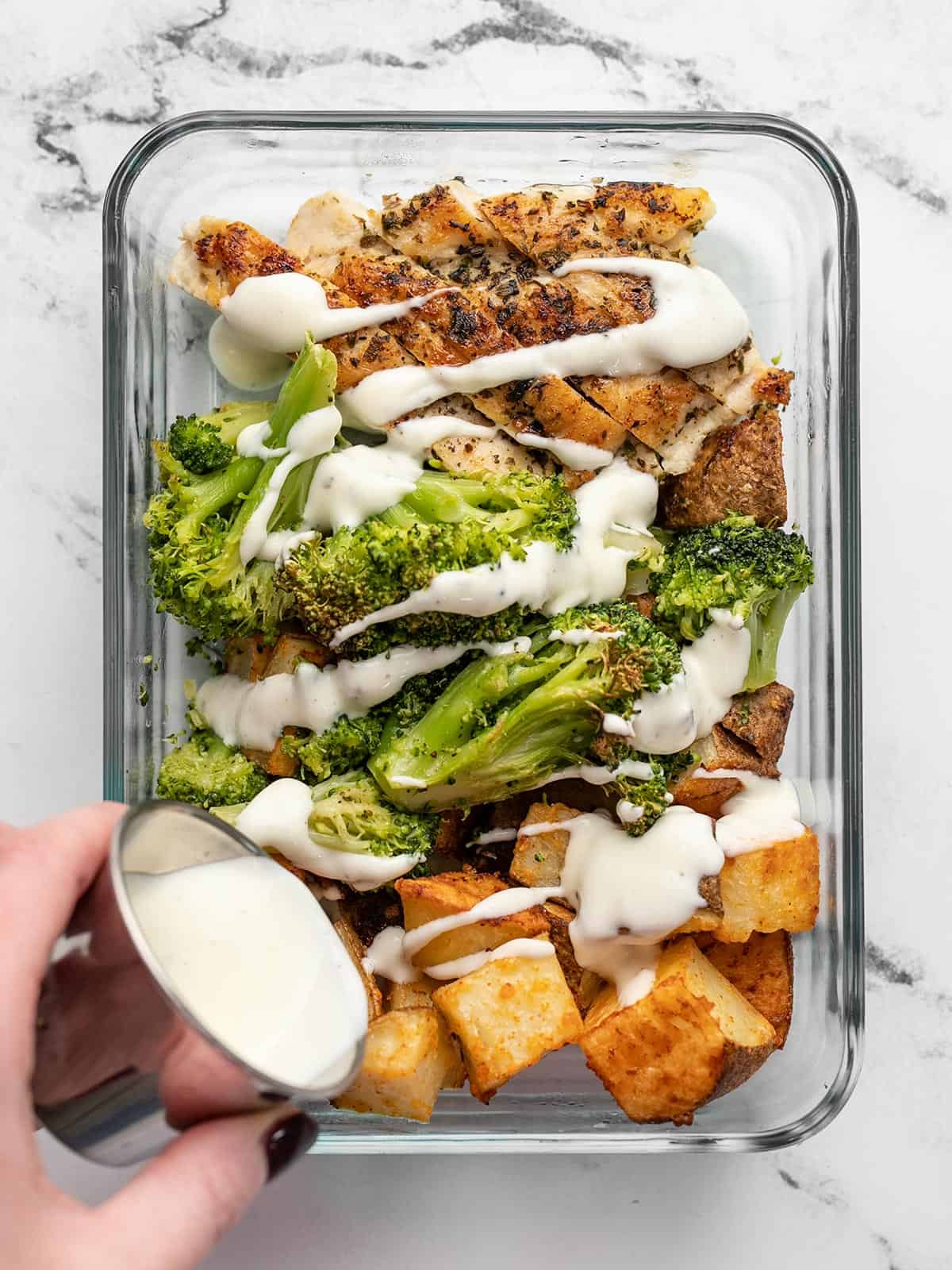 Overhead view of a ranch chicken meal prep container with ranch dressing being drizzled over top.