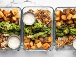 Three glass meal prep containers lined up in a row full of chicken, potatoes, and broccoli.