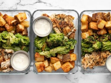 Three glass meal prep containers lined up in a row full of chicken, potatoes, and broccoli.