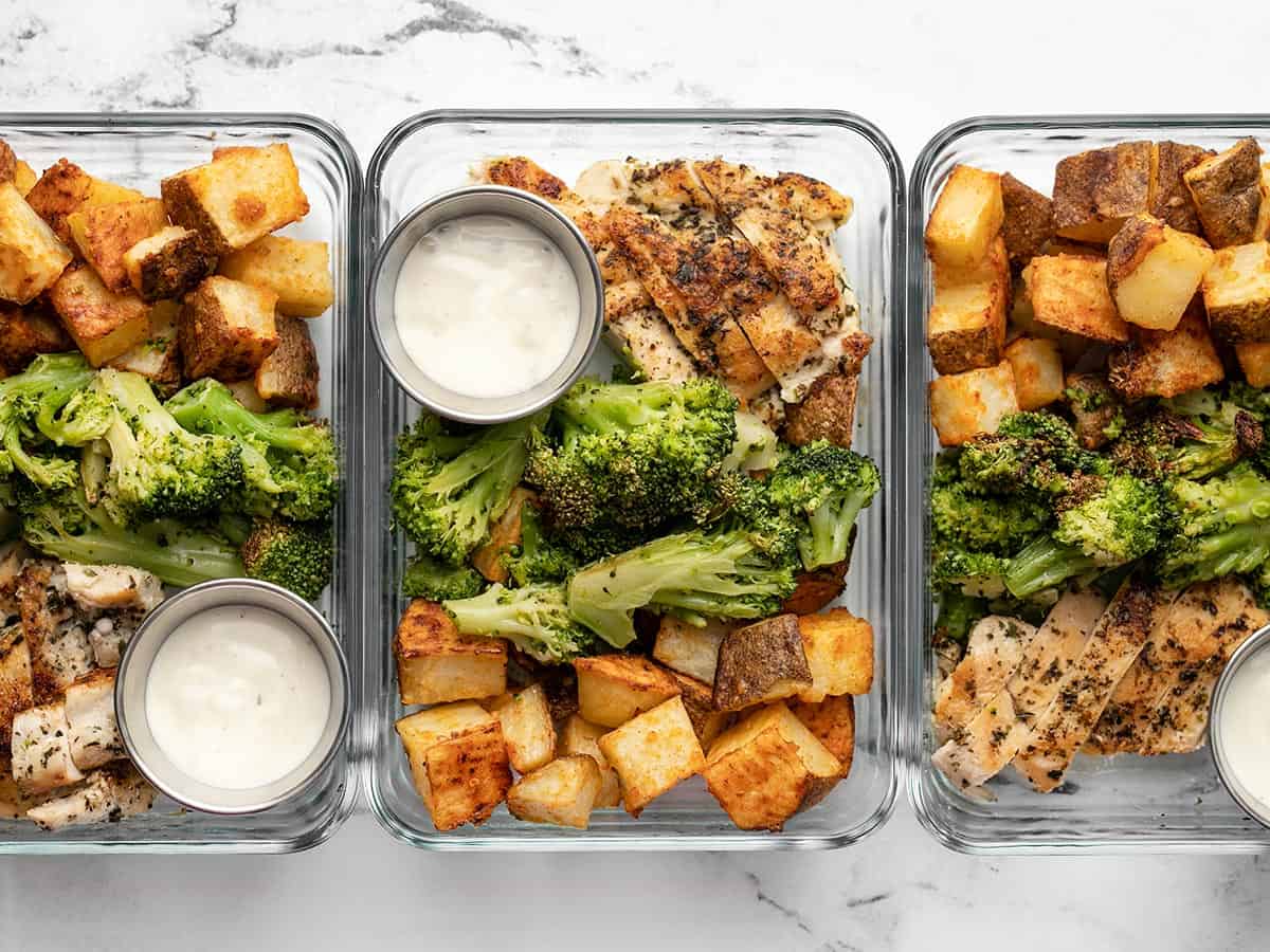 Three glass meal prep containers lined up in a row full of chicken, potatoes, and broccoli. 