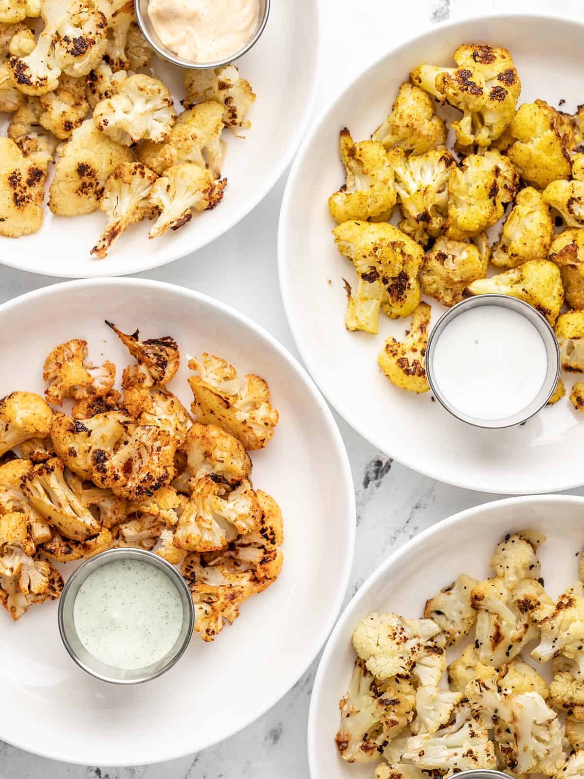 four plates of roasted cauliflower with dipping sauces.