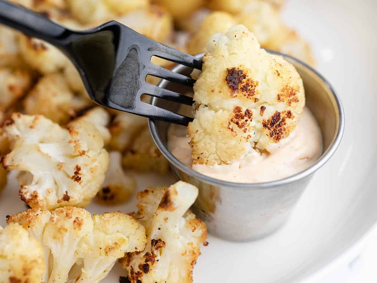 Roasted cauliflower being dipped into a dish of sauce.